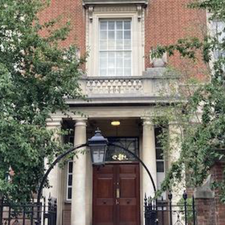 Photo of the Hopkins Building, Department of Biochemistry. It is a red brick building with an archway in front and trees framing the entrance