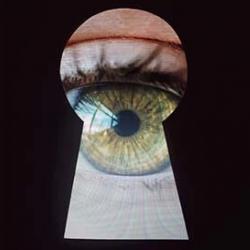 Stock photo of an eye looking through a keyhole. A black background masks a keyhole shape with a green eye peering through.