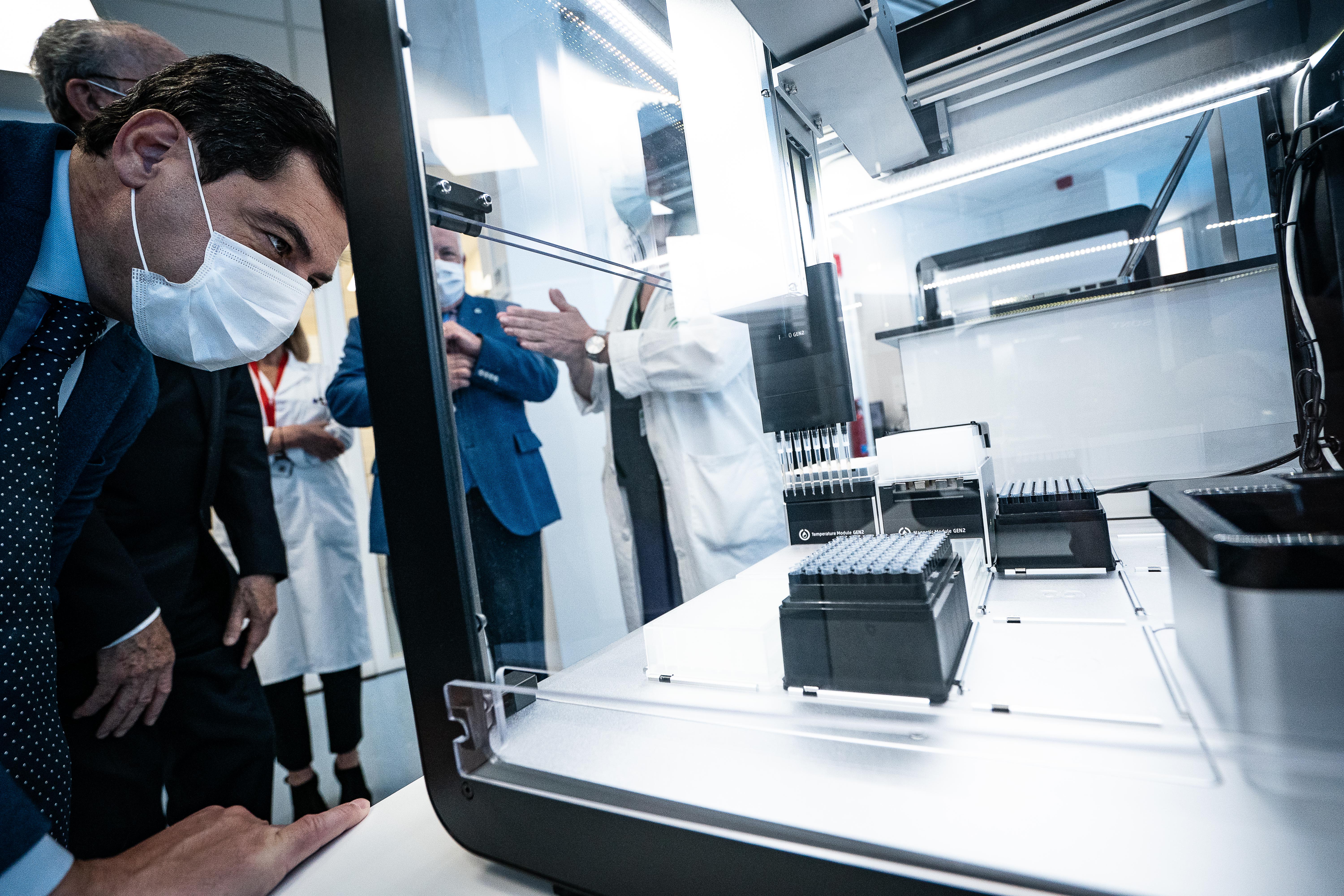 Photo of a man in a suit leaning over an OpenTron lab automation robot. The robot is using a multi-pipette to dispense liquid.