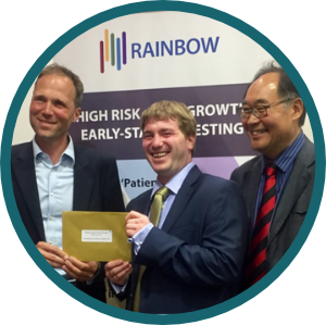 Three people stand in front of a banner with a gold envelop, they are smiling.