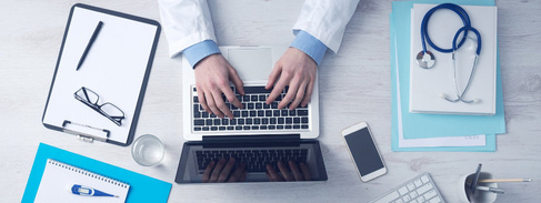 Top down photo of a doctor's desk with a set of hands typing on a computer