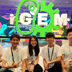 2023 Cambridge iGEM Team at the Jamboree in front of a huge iGEM logo