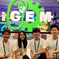 2023 Cambridge iGEM Team at the Jamboree in front of a huge iGEM logo