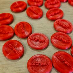 Photo of 3D printed disks with the word 'Autohaem' on them. The disks are bright red and look like blood cells.